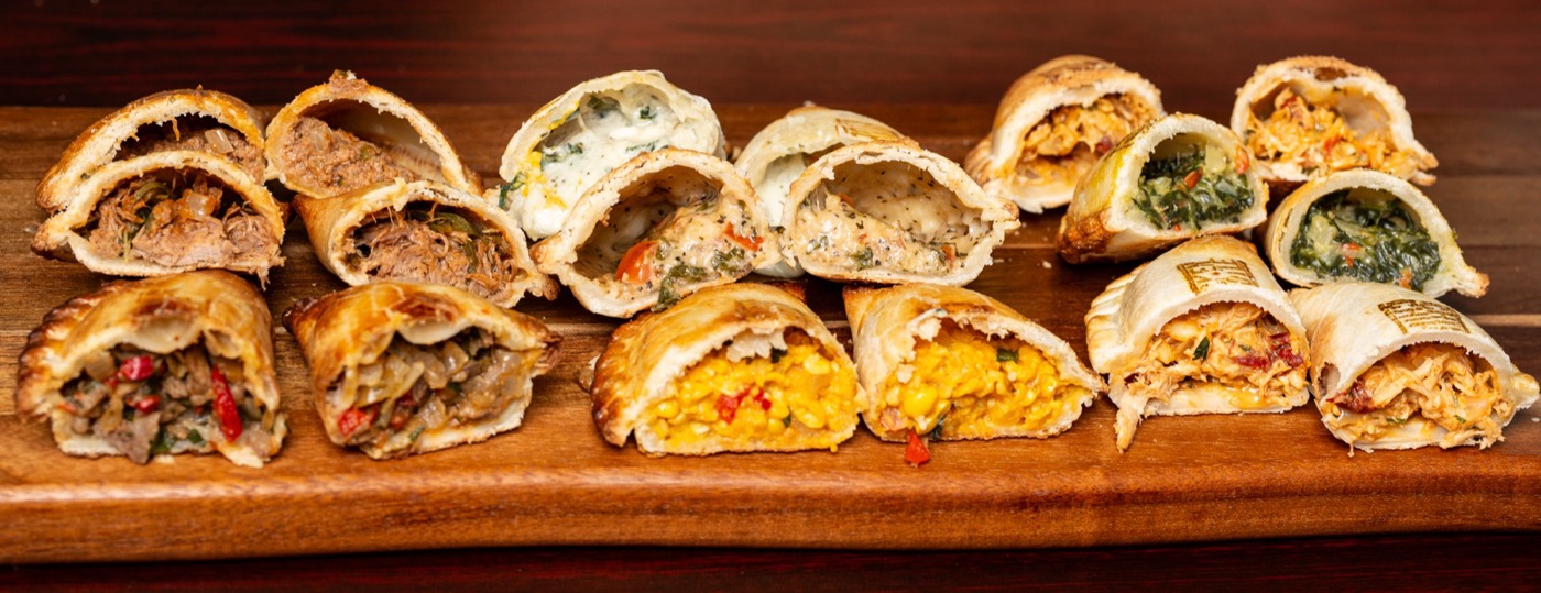 A long board of empanadas cut open, with dipping sauces