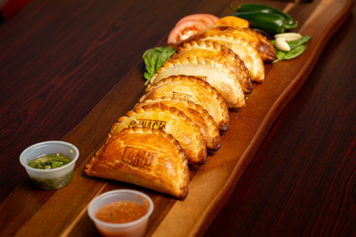 A long board of empanadas with dipping sauces